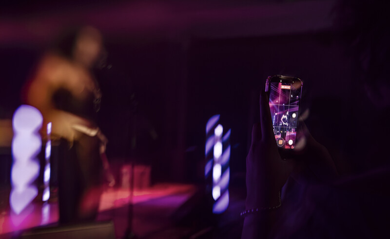 Smartphone displaying a vibrant purple LED interface during a performance with stage lighting and a performer visible in the background.