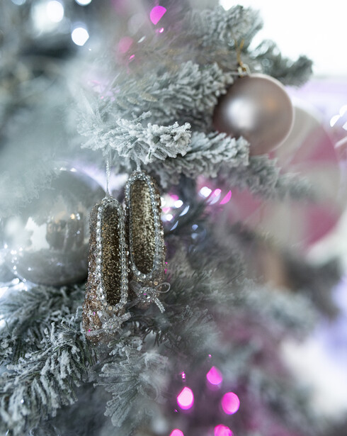 Frosted evergreen branch decorated with gold beads and magenta ornaments, shot with shallow depth of field.