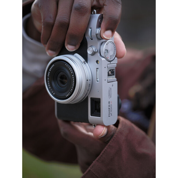Hands holding a silver rangefinder camera with fixed lens, viewed from above.