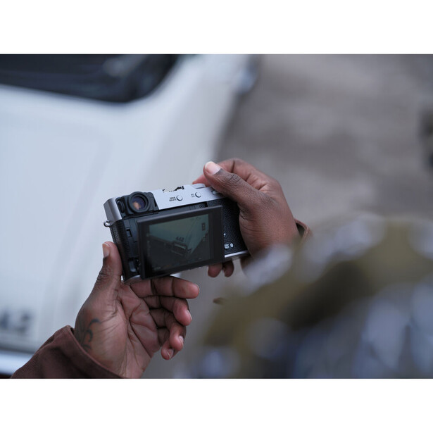 Photographer holding a vintage rangefinder camera with a view of unfocused urban scenery in the background.