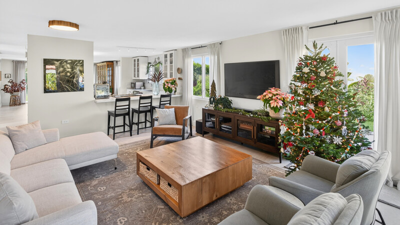 Bright, open-concept living room with decorated Christmas tree, neutral seating, and large television mounted above dark wood media console.