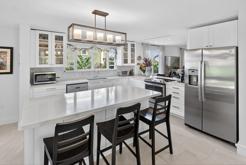 Modern kitchen with white cabinetry, stainless steel appliances, and a white quartz island with black seating.