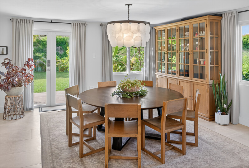 Modern dining room with round wooden table, four chairs, and large china cabinet near bright windows.