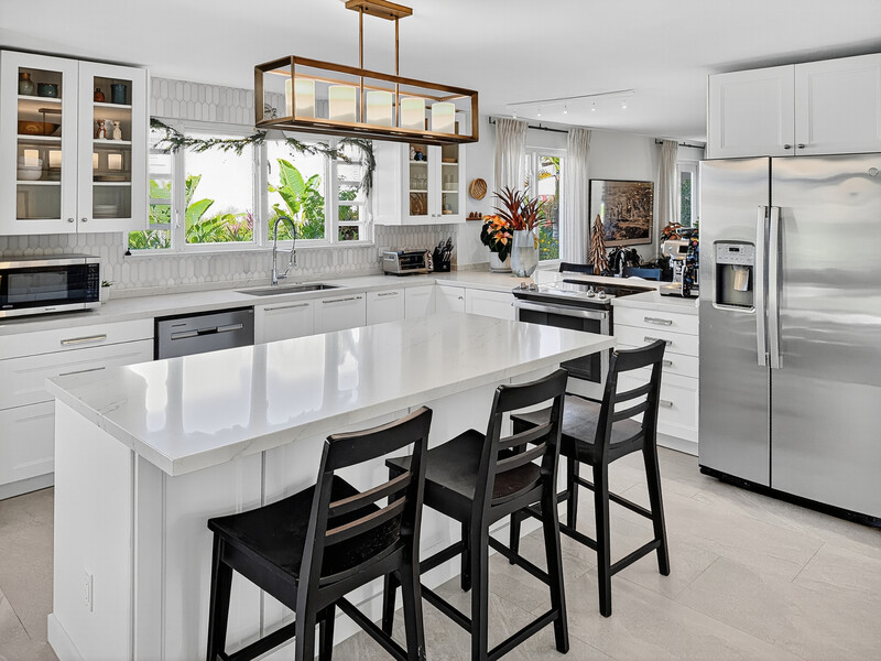 Modern white kitchen with island seating, stainless steel appliances, and natural light from large windows.