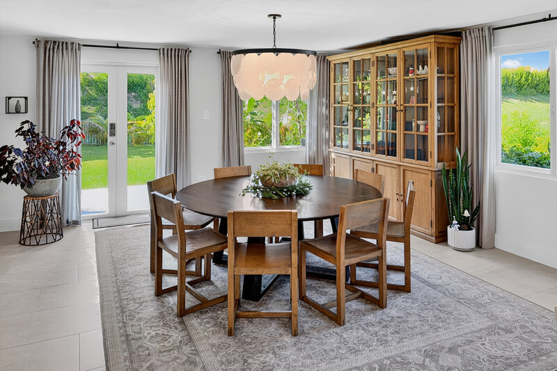 Modern dining room with round wooden table, four chairs, and large glass cabinet against natural daylight from windows.