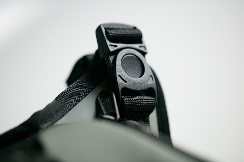 Close-up of a black camera strap with gray and silver buckle attachment against white background.
