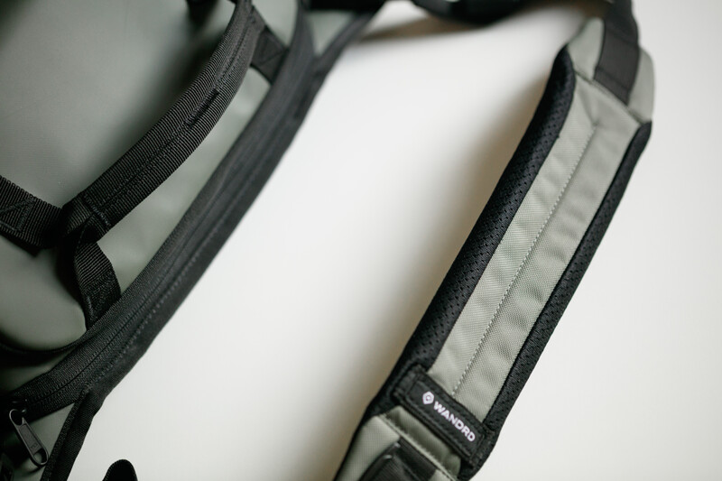 Close-up of camera strap attachment point with black nylon webbing and gray fabric detail against white background.
