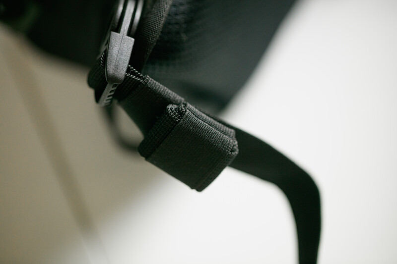 Close-up of black fabric straps with stitching and attachment hardware against a blurred white background.