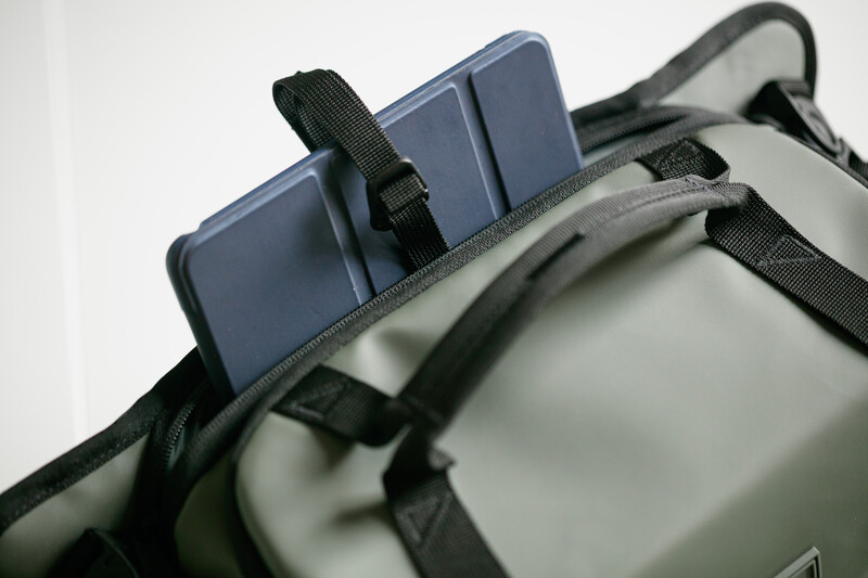 Blue smartphone mounted on gray camera bag with black straps using clip attachment.