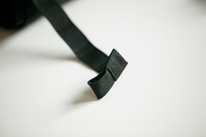 Close-up of a black fabric strap with a rectangular buckle or clasp detail against a white surface.