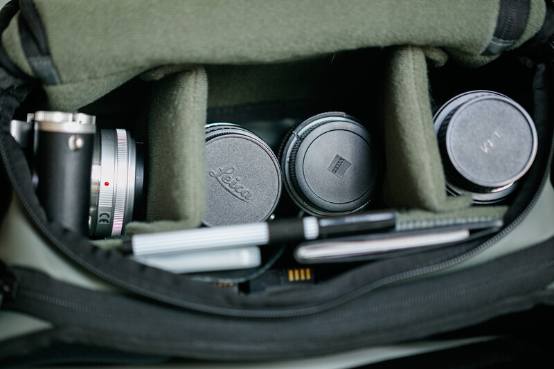 Camera bag interior with lens caps, a compact camera body, and accessories organized in padded compartments.