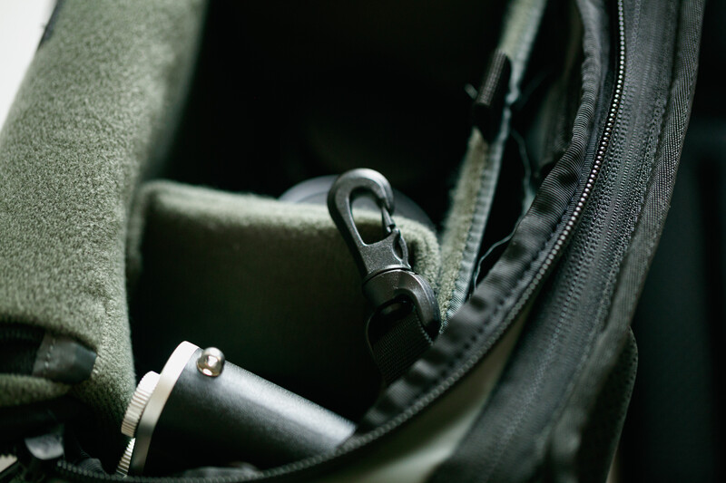 Close-up of camera gear inside an open olive-green camera bag with metal carabiners and padded compartments visible.
