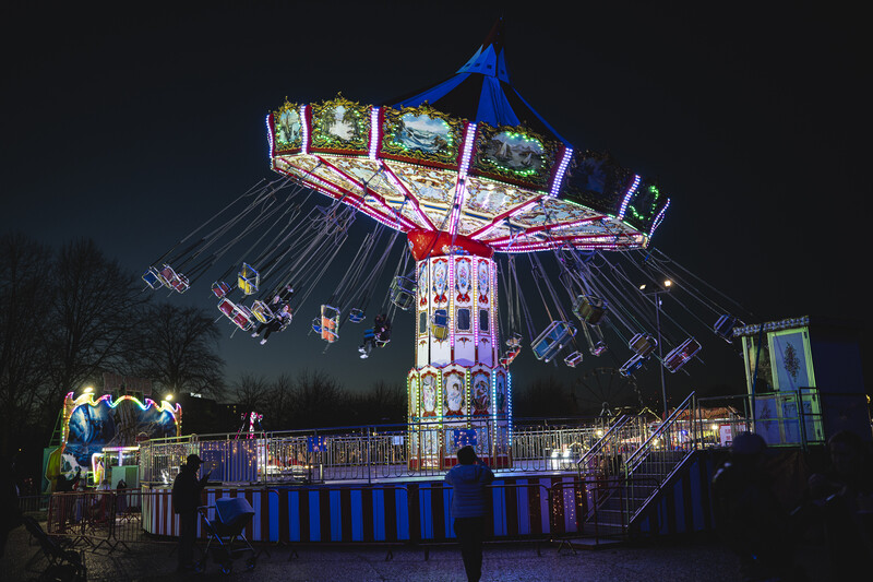 Illuminated carousel swing ride at night with blue canopy and colorful neon lighting throughout the amusement park setting.