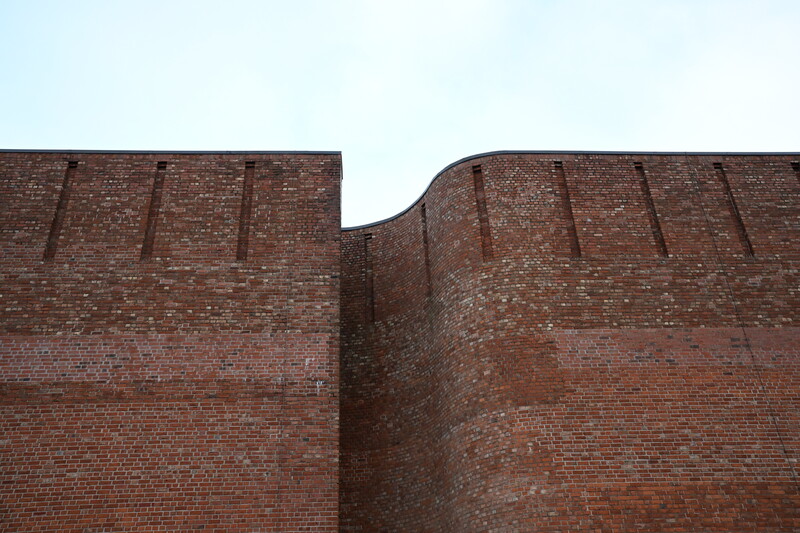 Two brick walls meeting at a right angle, showing weathered red and brown masonry against clear sky.