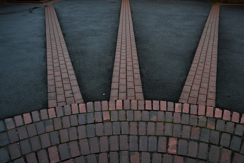 Overhead view of brick paving with three radiating pathways converging toward a curved archway pattern.