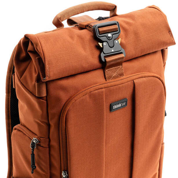 Orange canvas camera backpack with roll-top closure and side pockets against white background.