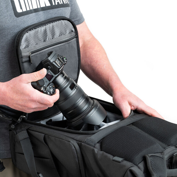 Photographer placing a telephoto lens into a shoulder camera bag while wearing a gray t-shirt.