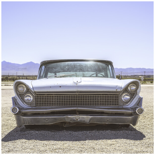 Front view of a vintage car with dual headlights and horizontal grille parked in an open desert landscape.