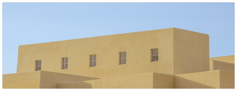Minimalist architectural photograph of a tan stucco building facade with five evenly spaced windows against clear blue sky.