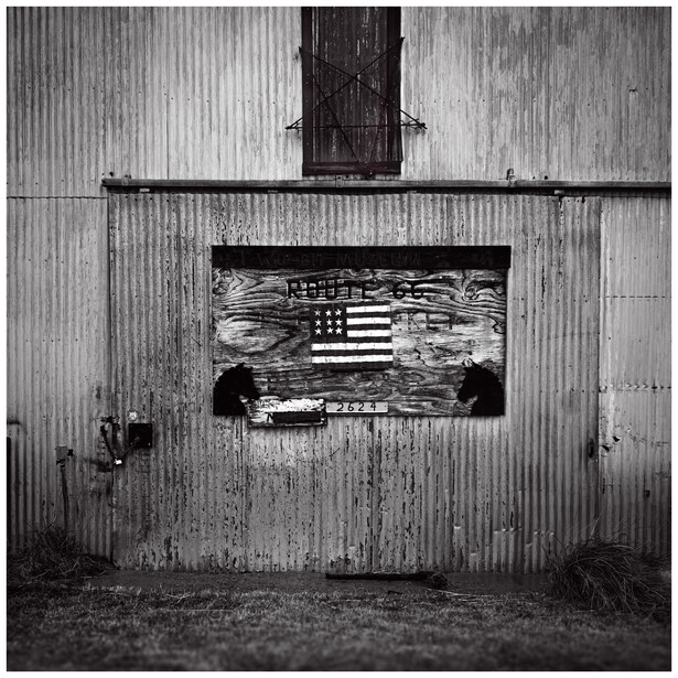 Weathered corrugated metal barn wall with American flag painted on wooden boards.