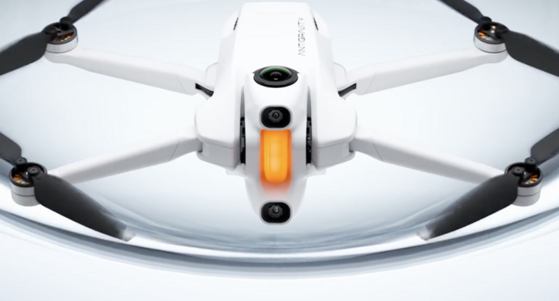 White drone with four black propellers and orange battery door viewed from above against white background.