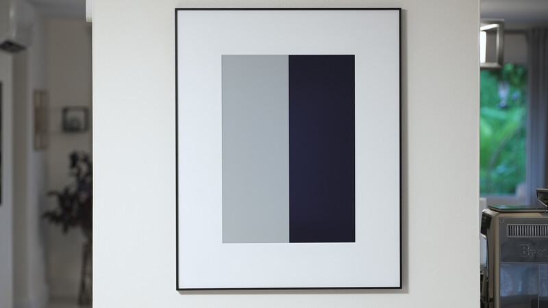 Framed abstract artwork with two vertical rectangular color blocks, one light gray and one dark navy, displayed on white wall.