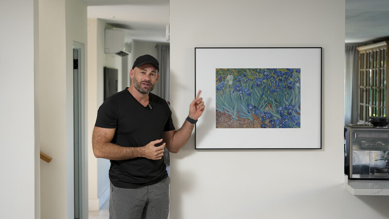 Man in black t-shirt pointing to framed Van Gogh Irises print on white wall in modern home interior.