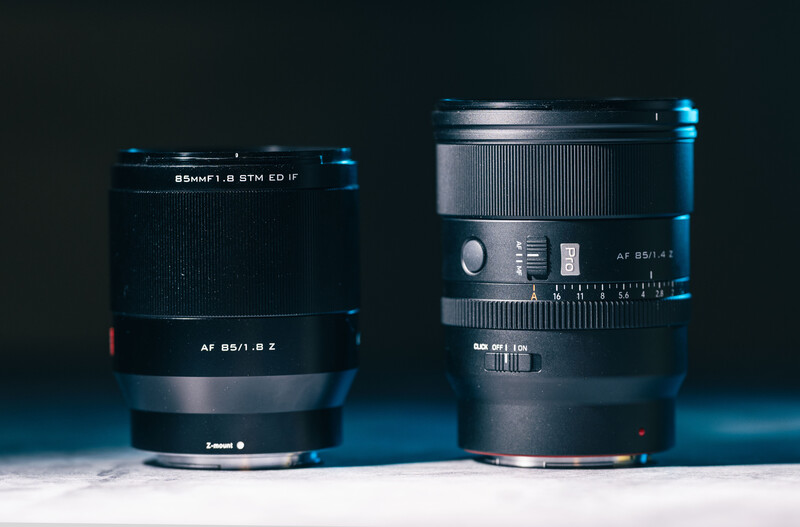 Two prime camera lenses with black barrels and focusing rings displayed side by side against a dark blue background.