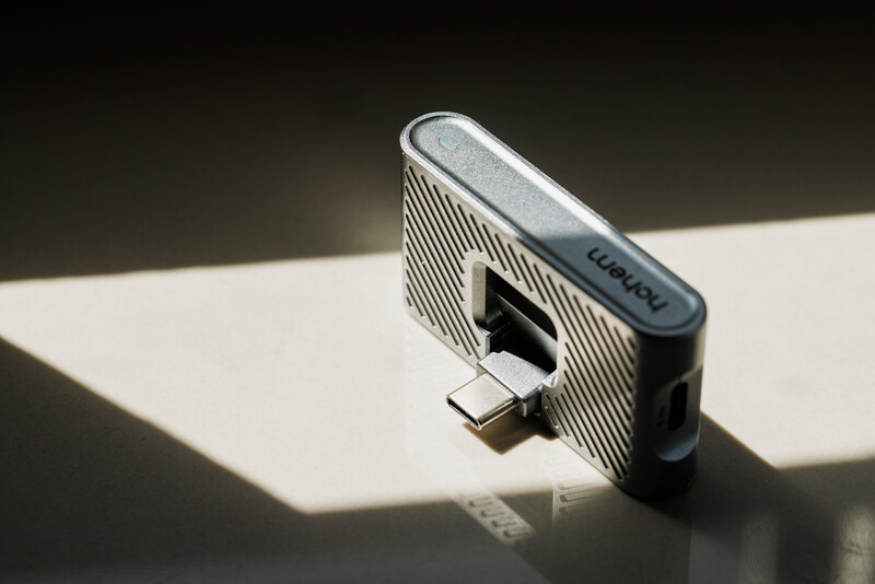 Compact external hard drive with ribbed casing and USB cable attached, positioned on white surface with dramatic side lighting.