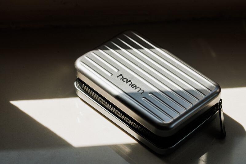 Silver ridged protective case with zipper lying on white surface under dramatic directional lighting.