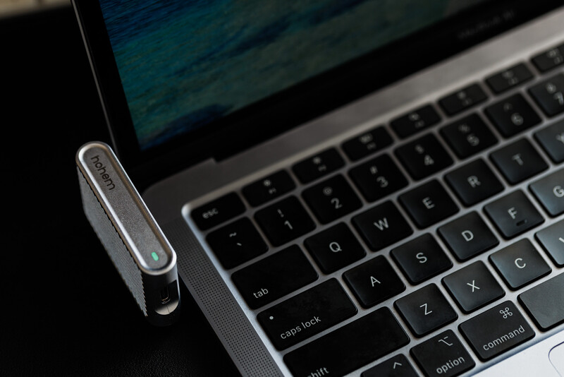 Silver wireless headset positioned next to a MacBook keyboard on a dark surface.