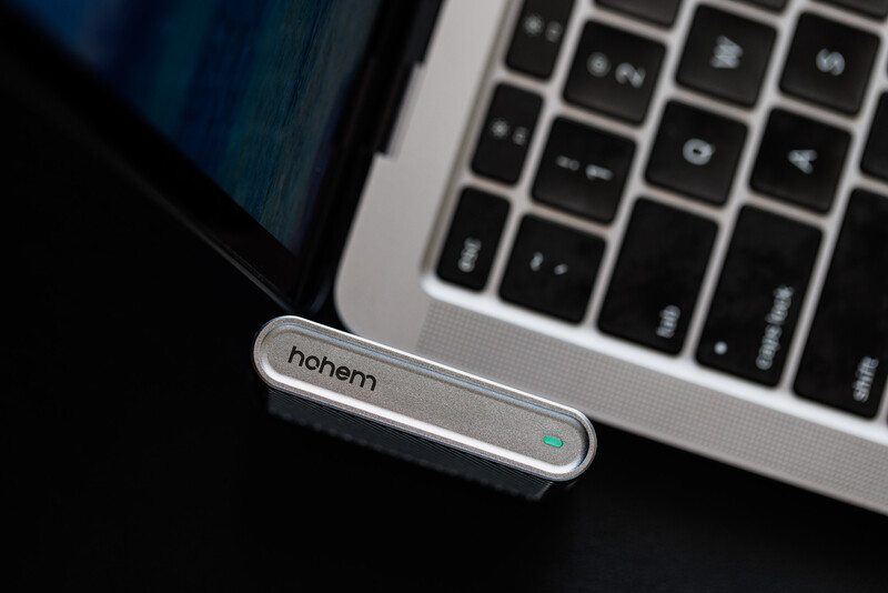 Hohem smartphone gimbal stabilizer positioned next to laptop keyboard on dark surface.