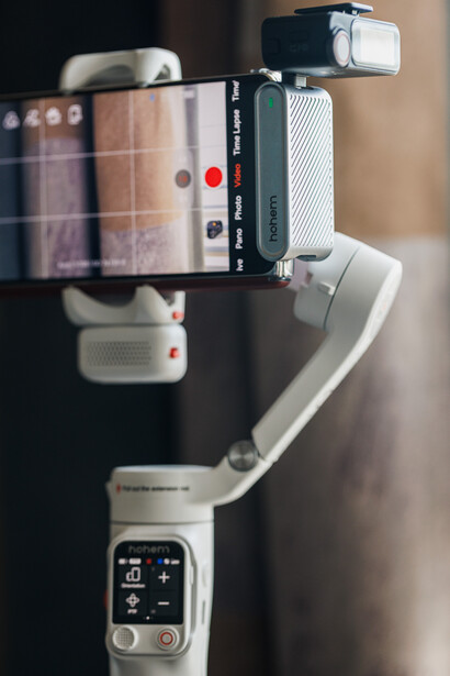 Smartphone gimbal stabilizer mounted on a tripod with smartphone attached to top arm.