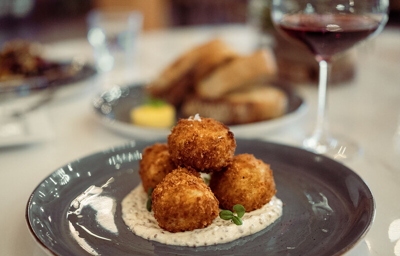 Three golden-brown fried spheres plated on creamy sauce with a dark rim plate.