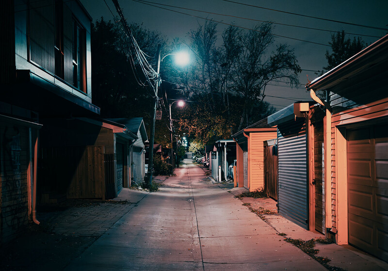 Night street lined with orange-walled buildings and streetlamp glow creating long shadows on pavement.