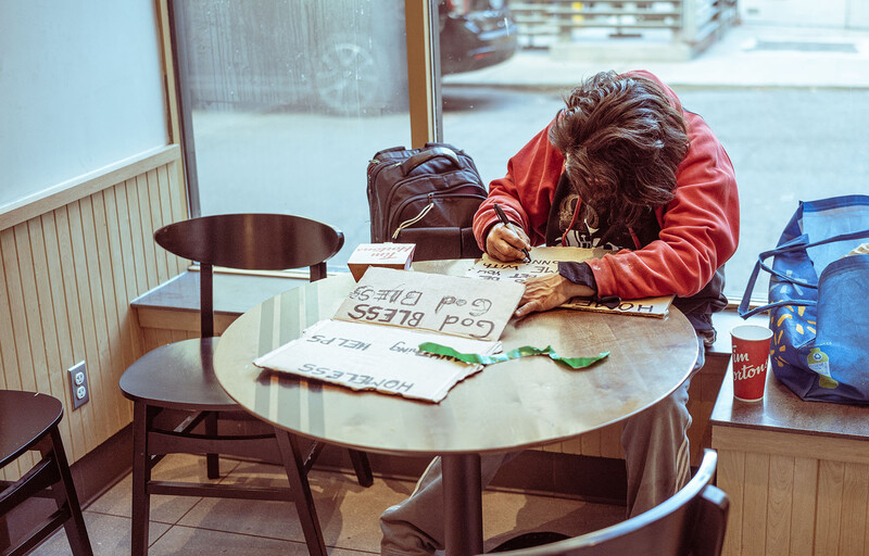 Person in red jacket leaning over round table studying architectural or design drawings and papers.