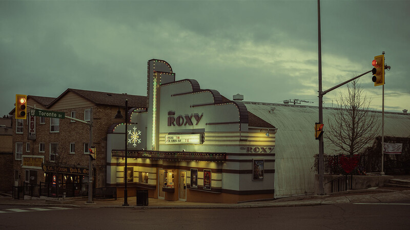 Art deco movie theater with illuminated marquee and vertical sign at dusk under overcast sky.