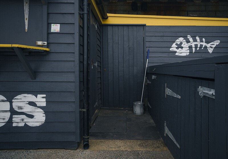 Narrow alleyway between dark wooden structures with white fish-shaped stencil art and yellow trim details.