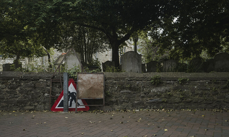 Street art sticker with warning triangle and figure on stone wall surrounded by trees.