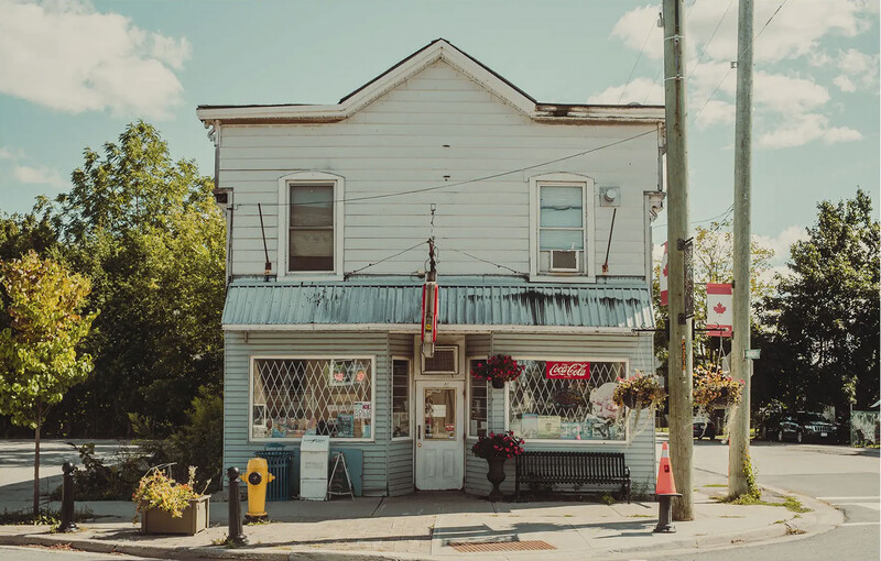 Two-story white wooden building with storefront windows and vintage Coca-Cola signage on a corner lot.