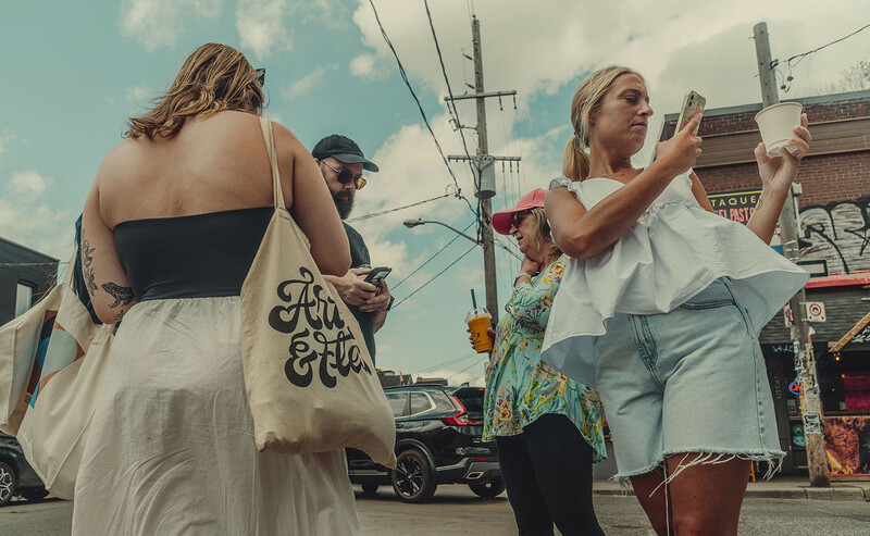 Woman with visible back tattoo taking a selfie on an urban street during daytime.