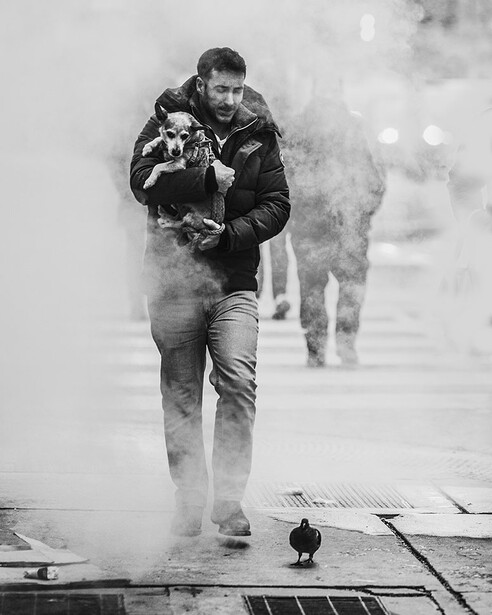 Man running through steam or smoke on a wooden boardwalk, holding a camera, shot in black and white.