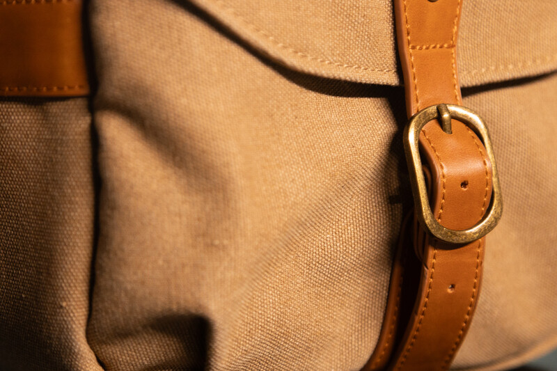 Close-up of tan canvas bag with cognac leather strap and brass ring hardware.