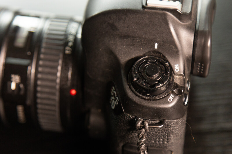 Close-up of a DSLR camera body showing the mode dial and grip texture with a lens visible in soft focus.