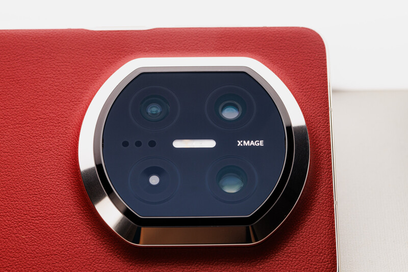 Quad camera module with metallic ring mounted on red textured smartphone back.