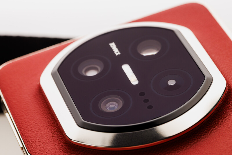 Close-up of a smartphone's camera module with four lenses arranged in a square formation on a red leather surface.