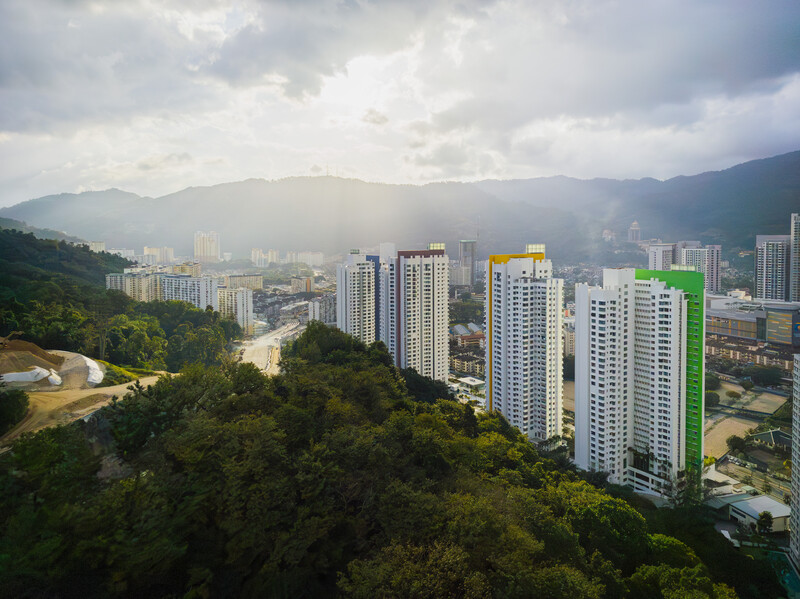 Aerial view of modern high-rise apartment buildings nestled in a forested valley with mountains in the background.