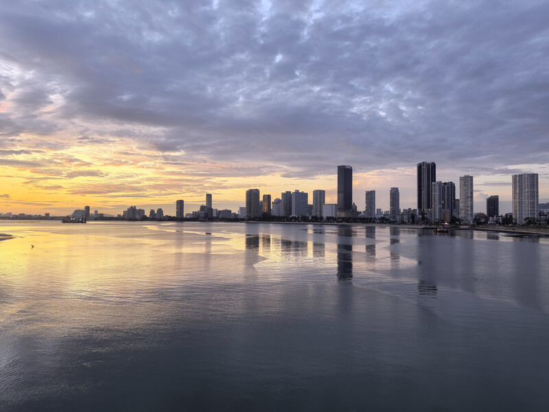 Waterfront cityscape at twilight with downtown skyline reflected in calm water under dramatic clouds.