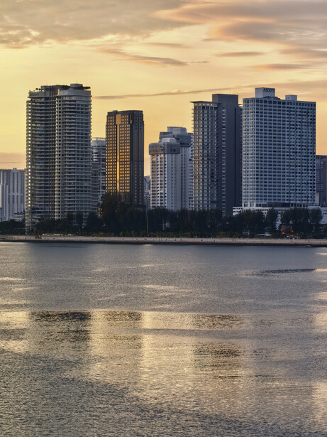 Urban skyline with high-rise buildings reflected in calm water at golden hour.