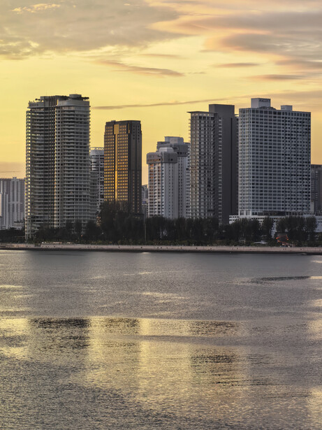 Skyline of high-rise buildings reflected in still water at golden hour.